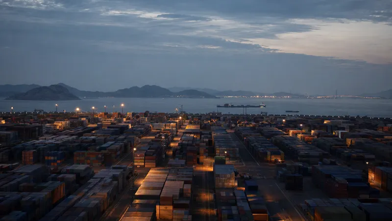 Ordered stacks of shipping containers at a large Asian port at blue hour, the sea and a moored ship in the distance